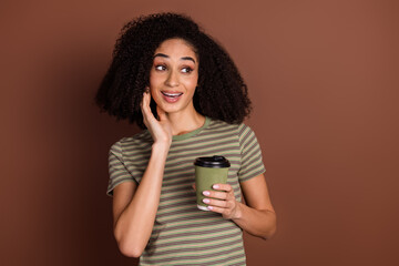 Poster - Photo of charming excited girl wear striped t-shirt arm cheek drink tea looking empty space isolated brown color background