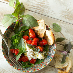 Wall Mural - plate of stracciatella cheese with baked cherry tomatoes and basil on a light table