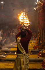 Wall Mural - Ganga aarti, Portrait of young priest performing holy river ganges evening aarti at assi ghat in traditional dress with hindu rituals at dashashwamedh ghat.