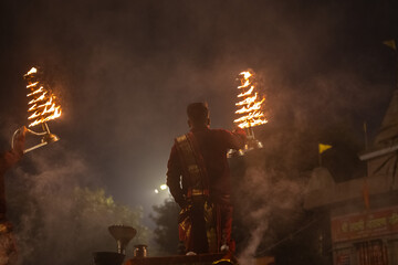 Wall Mural - Ganga aarti, Portrait of young priest performing holy river ganges evening aarti at assi ghat in traditional dress with hindu rituals