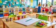 © Man888 - Colorful kindergarten classroom background with various children's artwork and toys, a clipboard with papers and a pen lie on a table, indicating a teacher's presence.