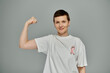 © LIGHTFIELD STUDIOS - A woman with short hair flexes her bicep, wearing a white t-shirt with a pink ribbon symbolizing breast cancer awareness.