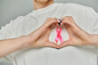 © LIGHTFIELD STUDIOS - Short-haired woman in white shirt forms heart with hands, emphasizing pink ribbon for breast cancer awareness