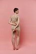 © LIGHTFIELD STUDIOS - A woman with short hair, wearing a beige bra stands facing away from the camera in a pink studio.