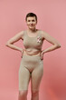 © LIGHTFIELD STUDIOS - A woman with short hair stands confidently in a bra and shorts, a pink ribbon pinned to her chest.