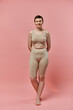© LIGHTFIELD STUDIOS - A woman with short hair stands in a pink bra with a pink ribbon pinned to it against a pink backdrop.