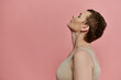 © LIGHTFIELD STUDIOS - A woman with short hair and a bra stands in profile against a pink background.