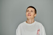 © LIGHTFIELD STUDIOS - A woman with short hair looks upwards, her white shirt adorned with a pink ribbon, a symbol of breast cancer awareness and prevention.