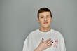 © LIGHTFIELD STUDIOS - A woman with short hair and a pink ribbon on her shirt, standing against a grey background.