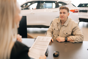 rear view of unrecognizable female manager giving car purchase documents to male buyer to review and