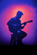© Tony Baggett - Purple silhouette of a male guitarist musician playing an acoustic guitar in an abstract music theme setting performing at a concert hall for a poster or flyer, musical stock illustration image