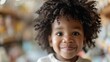 © familymedia - A young child with curly hair smiles brightly in an indoor setting, capturing an innocent and joyful moment, exuding warmth and happiness through their expression.