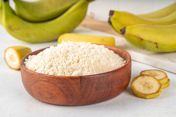 Wall Mural - Alternative organic banana flour with fresh whole and sliced green bananas on white table background