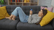 © Krakenimages.com - A relaxed young woman examines a credit card while lying on a gray sofa in a well-decorated home interior.