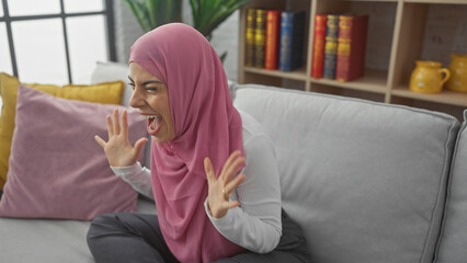 Wall Mural - A young, hispanic woman wearing a hijab is shouting in her living room.