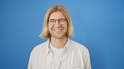 Poster - A smiling man with long blond hair and glasses posing against a blue background.