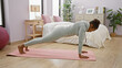 © Krakenimages.com - African american woman maintaining plank position on a yoga mat in a well-lit, cozy bedroom interior, conveying an atmosphere of healthy living.