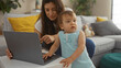 © Krakenimages.com - Woman with toddler using laptop in cozy living room reflecting family bonding and modern parenting, the intimate home setting with a baby girl adds warmth and affection to the scene.