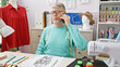 © Krakenimages.com - A mature man in glasses talks on the phone in a tailor shop surrounded by threads, mannequins, and a sewing machine.