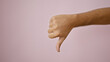 © Krakenimages.com - A young adult man's hand gestures a thumbs down against a pink background, expressing disapproval or rejection.