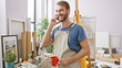 © Krakenimages.com - Smiling bearded man in apron talking on phone in art studio, holding red mug