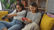 © Krakenimages.com - Two women enjoying a video game on a couch, evoking feelings of fun and togetherness in a cozy living room atmosphere.