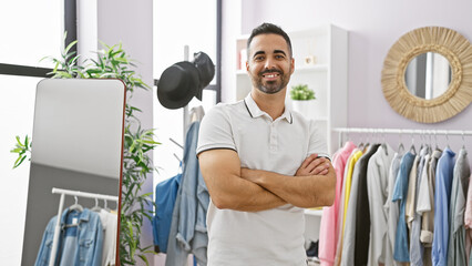 Wall Mural - Smiling young hispanic man with beard standing confidently in a modern clothing room indoors