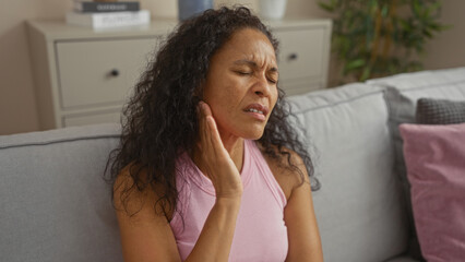 Woman experiencing pain while sitting on a couch in her living room, with a pained expression suggesting discomfort.