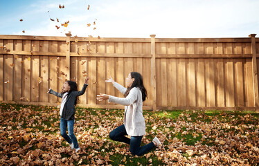 Wall Mural - Autumn, mother and daughter playing with leaves in garden of home together for bonding or love. Asian family, fall or throw with single parent woman and girl child having fun in backyard for games