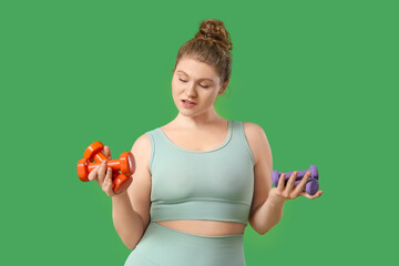 Sporty young woman with dumbbells on  green background