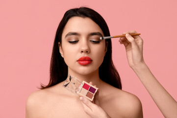 Poster - Female makeup artist working with young woman on pink background