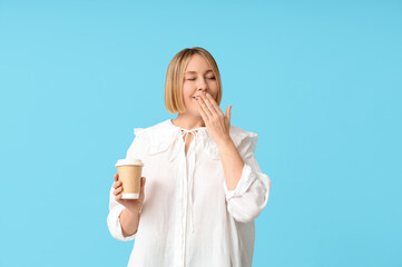 Wall Mural - Tired adult woman with paper cup of coffee on blue background