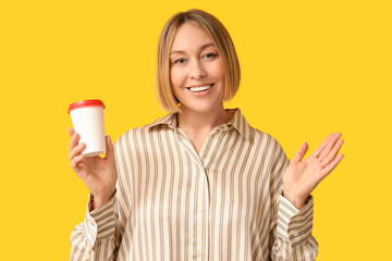 Wall Mural - Happy adult woman with paper cup of coffee on yellow background