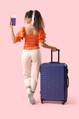 Wall Mural - Young African-American woman going somewhere with her baggage and passport with ticket on pink background. Back view