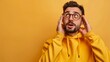 © Eleanor Richards - A man in a yellow hoodie looks surprised with his hands on his face, set against a yellow background, capturing a bright and dramatic moment of surprise.