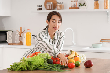 Poster - Young Asian woman taking tomato from counter in kitchen