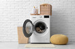 © Pixel-Shot - Modern washing machine with laundry, baskets and detergents near white brick wall