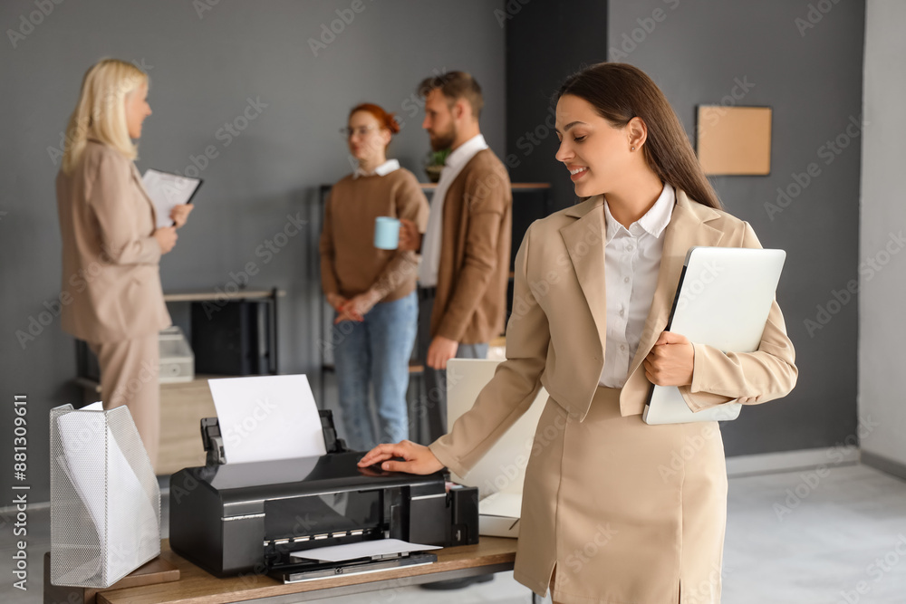 Young businesswoman with laptop using printer in office