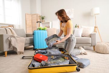 Wall Mural - Young woman packing her clothes into organizer at home. Travel concept