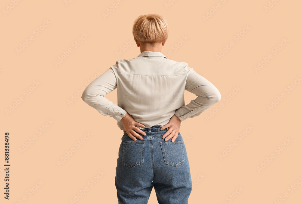 Mature woman suffering from back pain on beige background. Back view