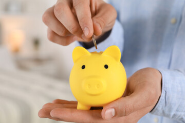 Poster - Man putting coin into yellow piggy bank indoors, closeup