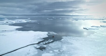 Wall Mural - Zodiac boat riding frozen polar ocean coast in Antarctica. Arctic snow covered landscape. People travel, explore South Pole wild winter nature. Science and tourist expedition. Aerial drone panorama