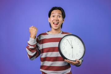 Happy Young Asian Man Wear Casual Style Clenched Fist And Rasied Hands Showing Victory Gesture While Holding Clock