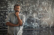 © Dinusha - A middle-aged man of diverse ethnicity stands before a blackboard wall filled with intricate doodles and mind maps, deep in thought. picture emphasize his mental struggle and overthinking.