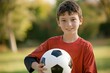 © kitipol - Boy in athletic attire, gripping a soccer ball and posing confidently