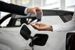 © sofiko14 - Dealer handing car key to businessman with electric SUV in background inside car dealership, symbolizing sustainable transportation, vehicle purchase, and business success.