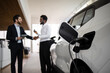 © sofiko14 - Dealer shaking hands with businessman after selling electric SUV in modern car dealership. Electric vehicle charging in foreground, signifying sale completion and eco-friendly transport.