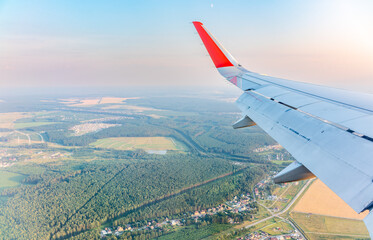 View of airplane wing, blue skies and green land during landing. Airplane window view.