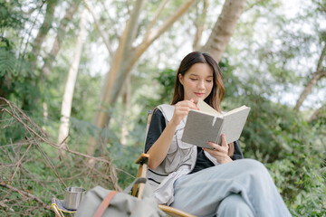 Poster - Asian girl sit on a camping chair, reading a book, relax on a relaxing day with nature