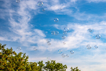 Colorful soap bubbles against blue sky with white clouds and trees at the edge of the picture. Background